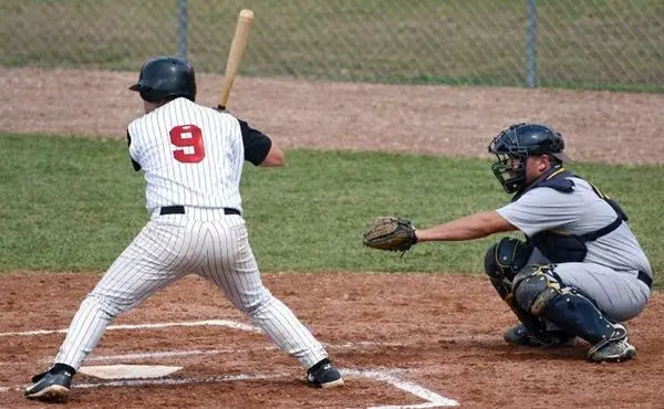 Батър удря топката на home plate с кетчър зад него по време на бейзболен мач